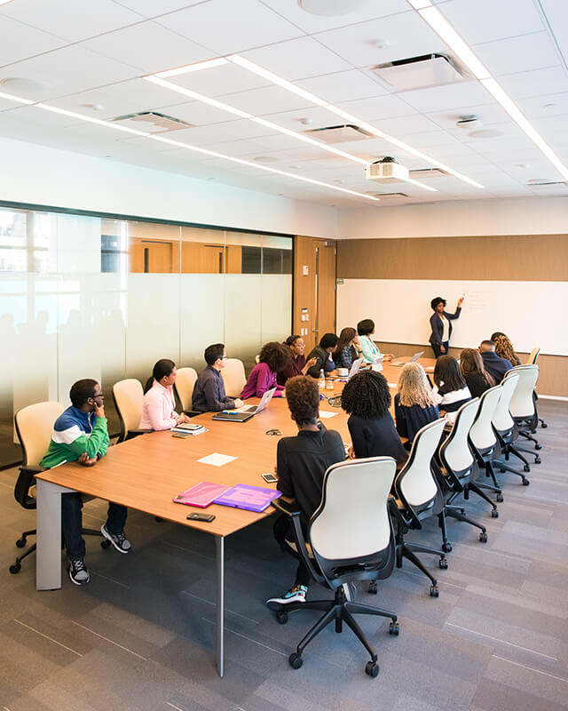 A team of people sittin at a long office table, paying attention to a whiteboard presentation.