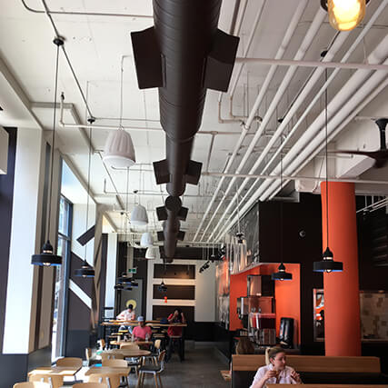 A restaurant with large black HVAC systems on the ceiling.